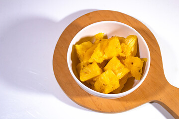 diced yellow pineapple on a porcelain bowl with a wooden cutting board