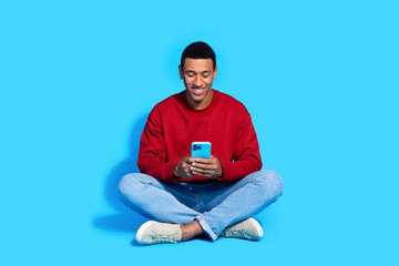 Photo of cheerful attractive man blogger sitting floor reading writing facebook telegram post...