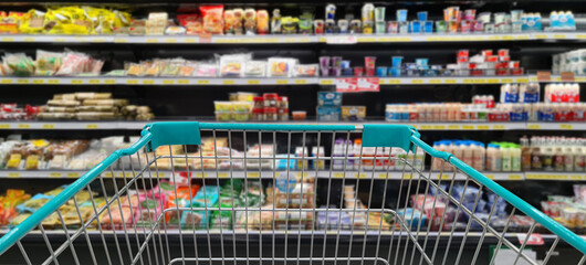 Green shopping cart with blurred image of grocery product on shelf in background. (Selective focused at shopping cart)