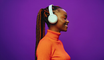 Young woman with trendy braids and purple background, listening to music with headphones - obrazy, fototapety, plakaty