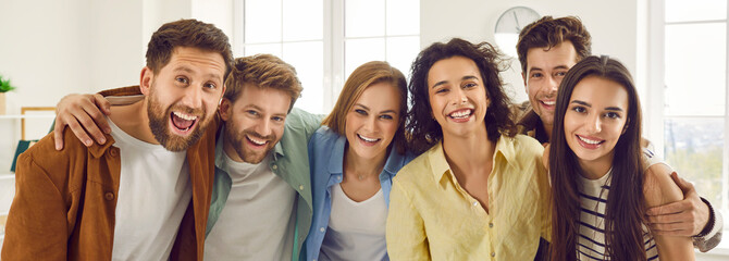 Group of happy smiling funny friends students or colleagues in casual clothes standing together and looking cheerful and positively at the camera. Portrait of friendly guys and girls indoors. Banner.
