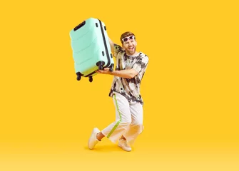 Foto op Canvas Full body photo of a funny young happy man in sunglasses carrying his blue suitcase is going on summer holiday trip and having fun on a yellow background. Vacation and travel concept. © Studio Romantic