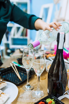 A woman waiter pours champagne from a bottle into a glass on a wooden table indoors at a banquet on a holiday. Food photography.