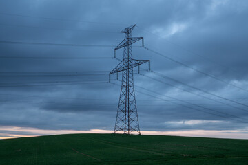 a tall power pole in the middle of a meadow under a cloudy sky