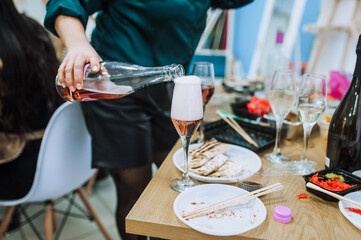 A woman waiter pours champagne from a bottle into a glass on a wooden table indoors at a banquet. Food photography.
