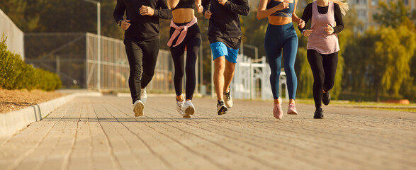 Cropped photo of legs of a people group in sportswear jogging along a path in the park having sport...