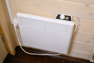White modern smart convector heater connected to an outlet on the wall of a wooden house. Smart...