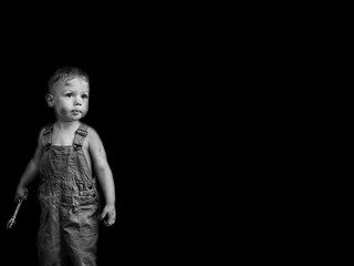 little boy in overalls with a wrench on a black background