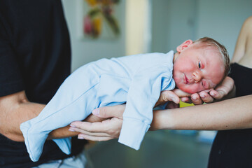 A newborn baby in the hands of his parents, clothes for a newborn baby. Cotton romper on a newborn boy.