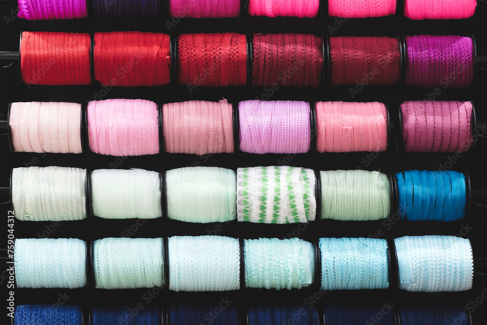 Aufkleber A row of colorful spools of thread, tape, braid  are displayed in a store. The spools are arranged in a rainbow pattern, with each color being represented in the display. spools are of various sizes