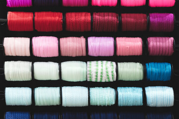 A row of colorful spools of thread, tape, braid  are displayed in a store. The spools are arranged in a rainbow pattern, with each color being represented in the display. spools are of various sizes