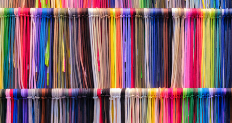 A row of colorful strings laces are displayed in a store. The colors are bright and vibrant,...