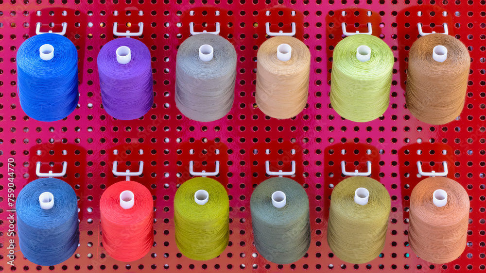Aufkleber A row of colorful spools of thread are displayed in a store. The spools are arranged in a rainbow pattern, with each color being represented in the display. The spools are of various sizes