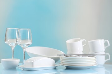 Fototapeta na wymiar Set of many clean dishware, cutlery and glasses on light blue table