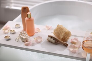 Fototapeta na wymiar Wooden tray with toiletries and flower petals on bathtub in bathroom