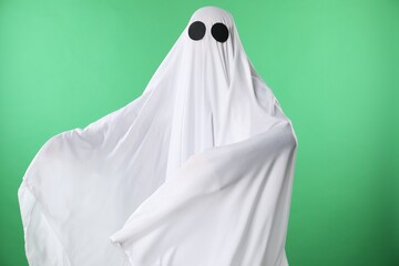 Creepy ghost. Person covered with white sheet on green background