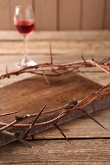 Crown of thorns and glass with wine on wooden table, selective focus
