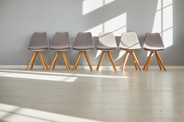 Front view of a row of modern empty chairs standing in corridor or conference room on a gray wall background in a minimal style. Waiting room interior in office. Interview, recruitment concept