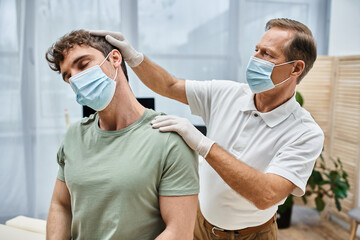 good looking mature doctor with mask and gloves helping his patient to rehabilitate in hospital