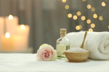 Obraz na płótnie Canvas Beautiful spa composition with essential oil, sea salt and rose on white towel against blurred lights. Space for text