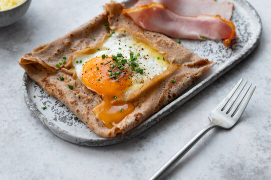 Homemade buckwheat crepes. Galettes bretonnes with cheese and fried egg on a gray background. Traditional French cuisine.
