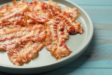 Delicious fried bacon slices on blue wooden table, closeup