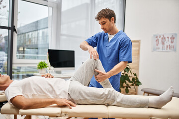 good looking dedicated doctor in blue robe helping his mature patient to rehabilitate in hospital
