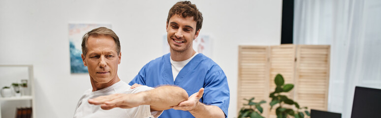cheerful handsome doctor helping his mature patient to stretch during rehabilitation, banner