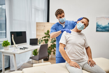 hardworking handsome doctor with mask stretching his patient during appointment in hospital