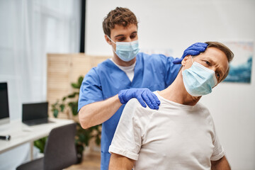 attractive doctor with medical mask and gloves helping his patient to stretch during appointment