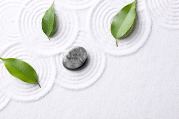 Zen garden stones and green leaves on white sand with pattern, flat lay. Space for text