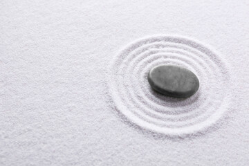 Fototapeta na wymiar Zen garden stone on white sand with pattern, above view. Space for text