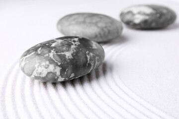 Zen garden stones on white sand with pattern, closeup