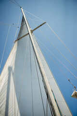 the white sail of the yacht against the background of a clear blue sky.