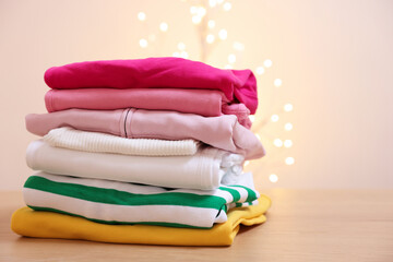 Stack of folded clothes on wooden table against beige background with blurred lights. Space for text