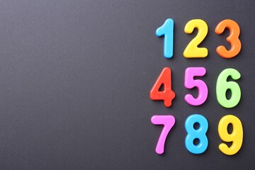 Colorful numbers on dark gray background, flat lay. Space for text