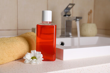 Fresh mouthwash in bottle, chamomile and towel on countertop near sink in bathroom, closeup