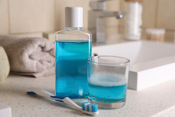 Fresh mouthwash in bottle, glass and dental floss on countertop in bathroom, closeup