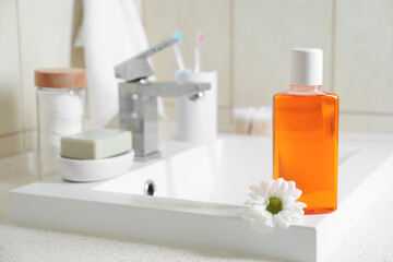 Fresh mouthwash in bottle and chamomile on sink in bathroom, closeup. Space for text