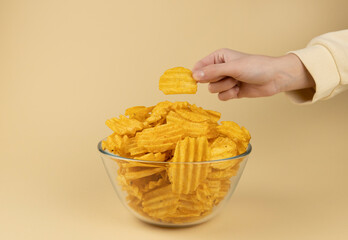The hand takes potato chips from the glass bowl. The hand with the chips.