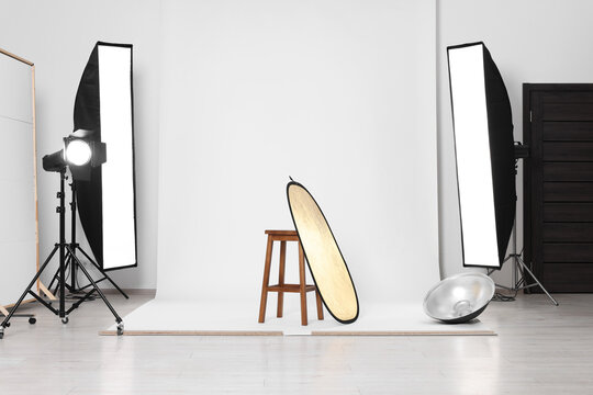 Stool with light reflector, professional lighting equipment and white background in photo studio
