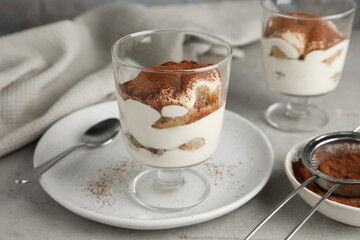 Delicious tiramisu in glass and sieve with cocoa powder on light table