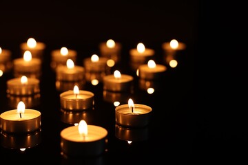 Burning candles on mirror surface in darkness, closeup. Space for text