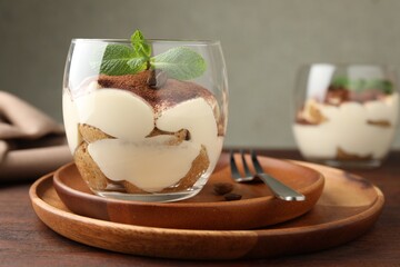Delicious tiramisu in glass, mint leaves, coffee beans and fork on wooden table, closeup