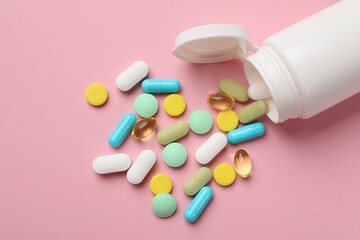 White bottle and different vitamin pills on pink background, top view