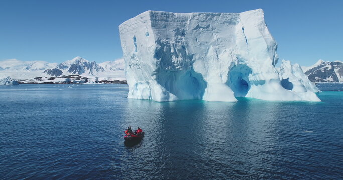People boat tour expedition to Antarctic iceberg. Antarctica travel and exploration. Arctic winter glacier drift ocean. Pristine South Pole landscape, sunny day. Aerial drone flight panoramic