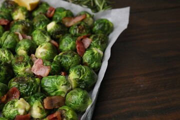 Delicious roasted Brussels sprouts and bacon in baking dish on wooden table, closeup. Space for text