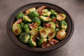 Delicious roasted Brussels sprouts and bacon in bowl on brown table, closeup