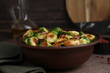 Delicious roasted Brussels sprouts and bacon in bowl on brown table, closeup