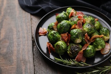 Delicious roasted Brussels sprouts, bacon and rosemary on wooden table, closeup. Space for text